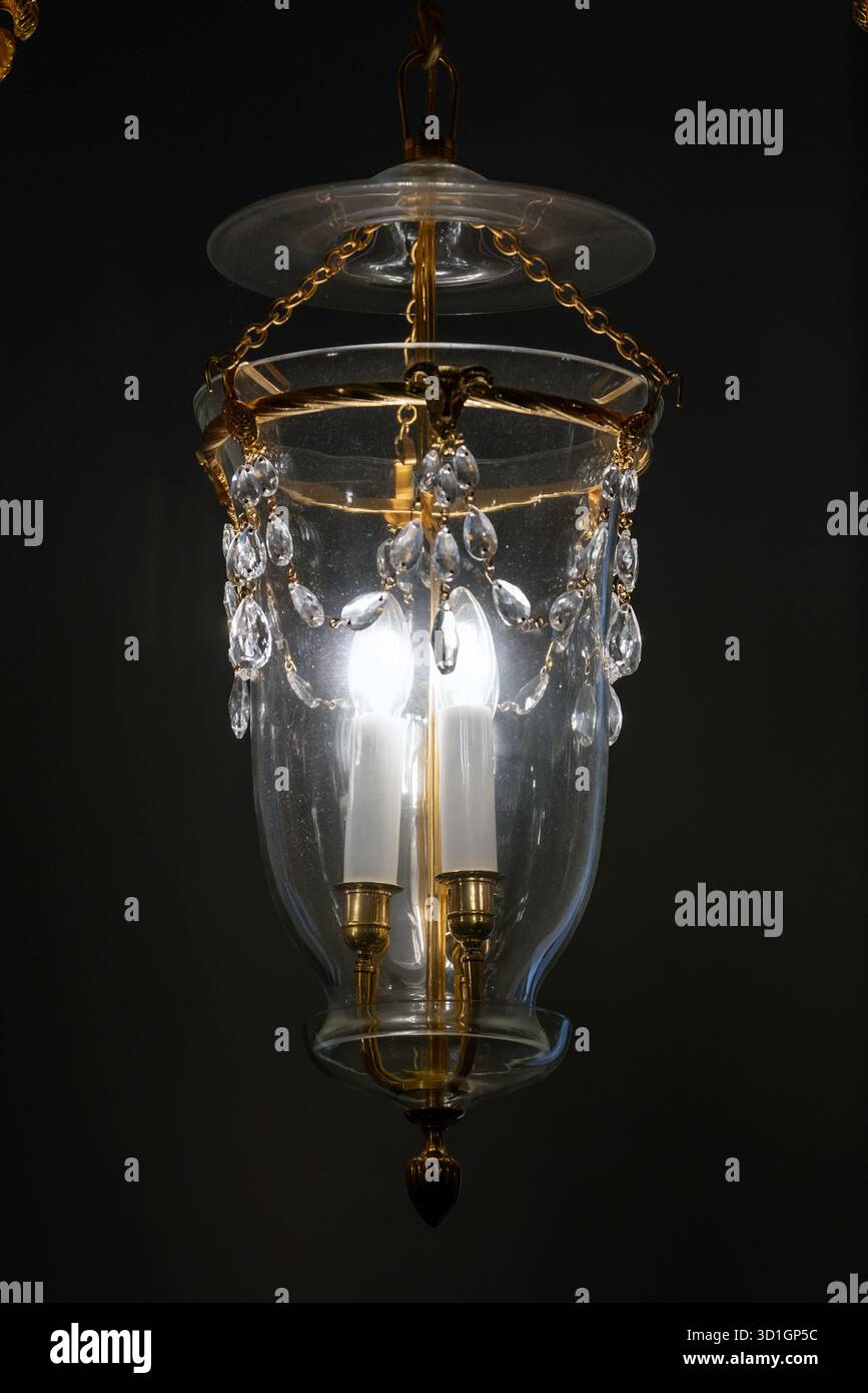 Un raffinato lampadario a lanterna di vetro sospeso da catene d'oro, caratterizzato da perle di cristallo e lampadine in stile candela che emettono un caldo bagliore. Perfetto per il lusso Foto Stock