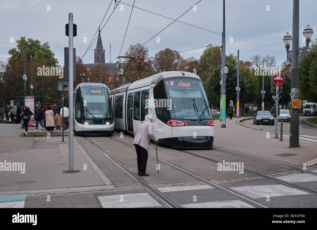 Donna anziana con bastone che attraversa la strada di fronte ai tram in Place de la Republique Strasburgo Foto Stock