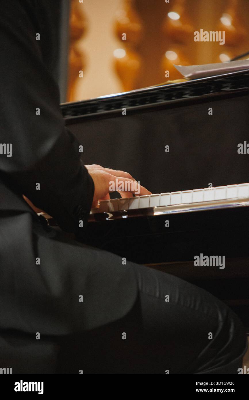 Un uomo che indossa un abito impeccabile su misura suona con maestria e passione un pianoforte incredibilmente bello che affascina il pubblico Foto Stock