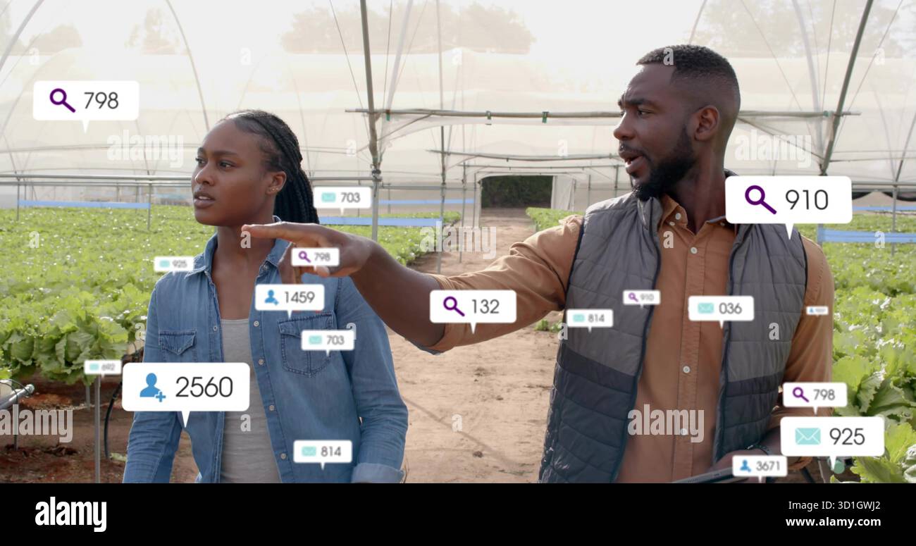 Il duo di tecnici a piedi ispeziona i vassoi idroponici in serra ad arco, con sovrapposizioni di dati Foto Stock