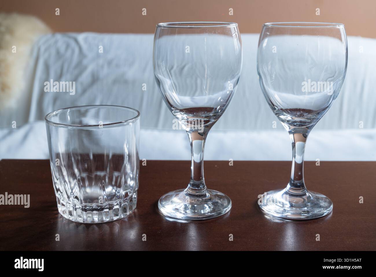 Tre bicchieri da bere vuoti, uno corto bicchierino a fantasia e due bicchieri da vino a stelo, sono disposti in modo ordinato su una superficie in legno scuro e lucido Foto Stock