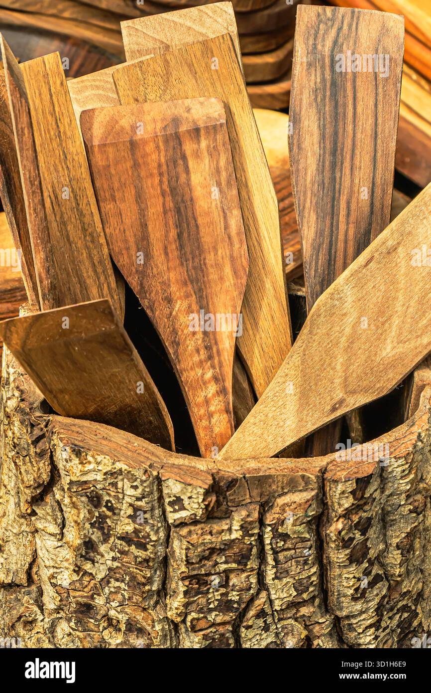 Una collezione di spatole in legno fatte a mano disposte ordinatamente in un supporto per corteccia. L'immagine cattura l'artigianato tradizionale, le texture naturali e il rus' Foto Stock