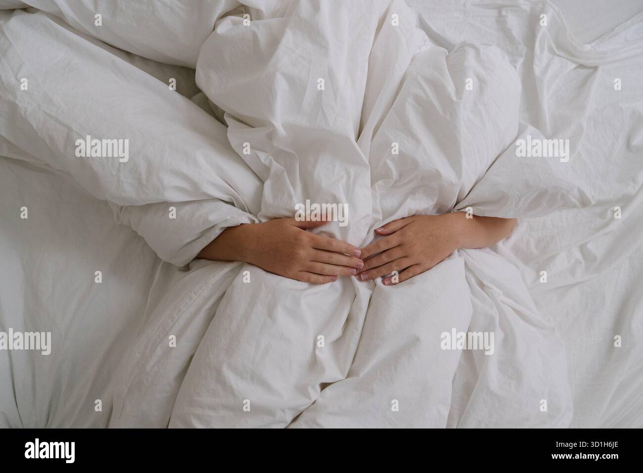 Ambiente accogliente con mani appoggiate sotto soffici letti bianchi. Estetica minimalista che simboleggia il comfort, il relax, il riposo e il sonno tranquillo. Foto Stock