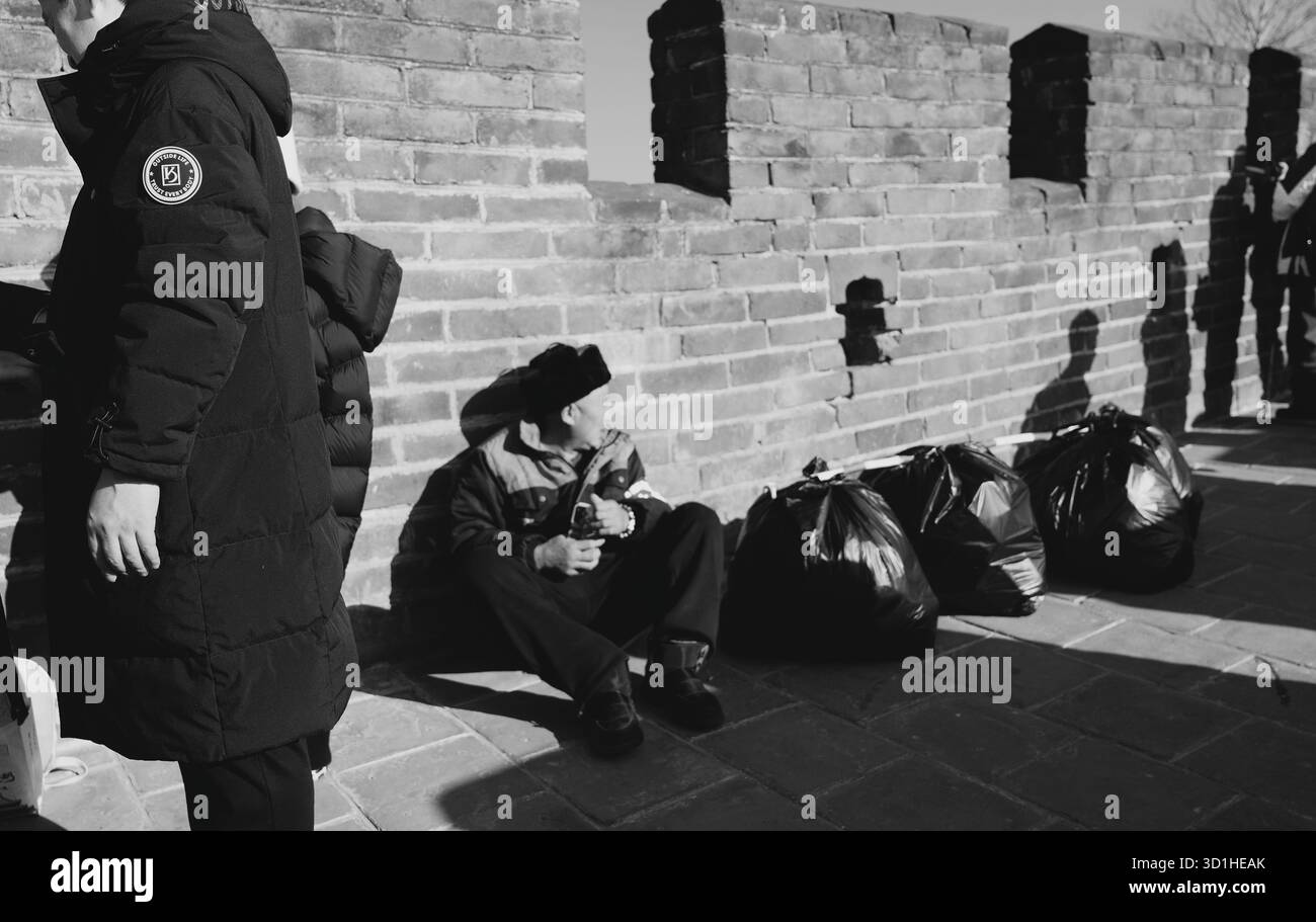 Lavoratore fuori fuoco seduto accanto ai sacchi della spazzatura sulla grande Muraglia Foto Stock