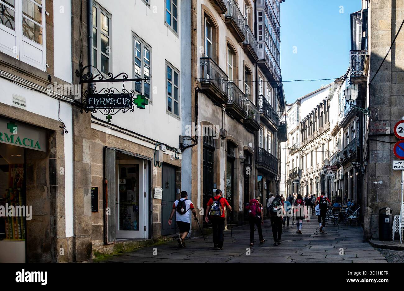 I pellegrini con zaini camminano attraverso una stretta strada storica di Santiago de Compostela, Galizia, Spagna, passando davanti alle farmacie e ai caffè lungo il cammino Foto Stock