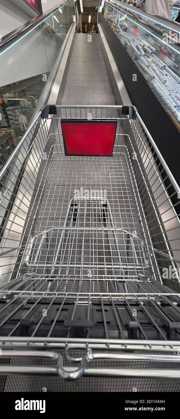 Carrello posizionato su una scala mobile, con un cartello rosso, circondato da un moderno spazio commerciale, che offre un'esperienza di shopping moderna. - Immagine stock catturata con smartphone