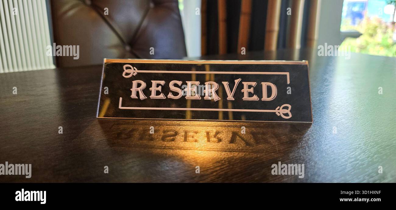 Insegna riservata posta su un tavolo in legno lucido, che mostra un decor elegante e luci soffuse, creando un'atmosfera sofisticata. Foto Stock