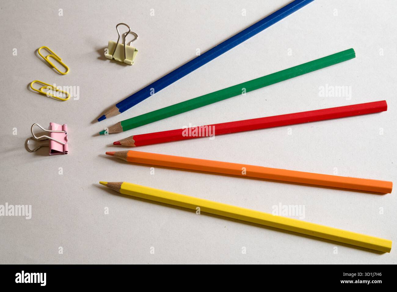 Una vivace disposizione di matite colorate, graffette metalliche e clip leganti, pronte per lo studio o il lavoro creativo. Foto Stock