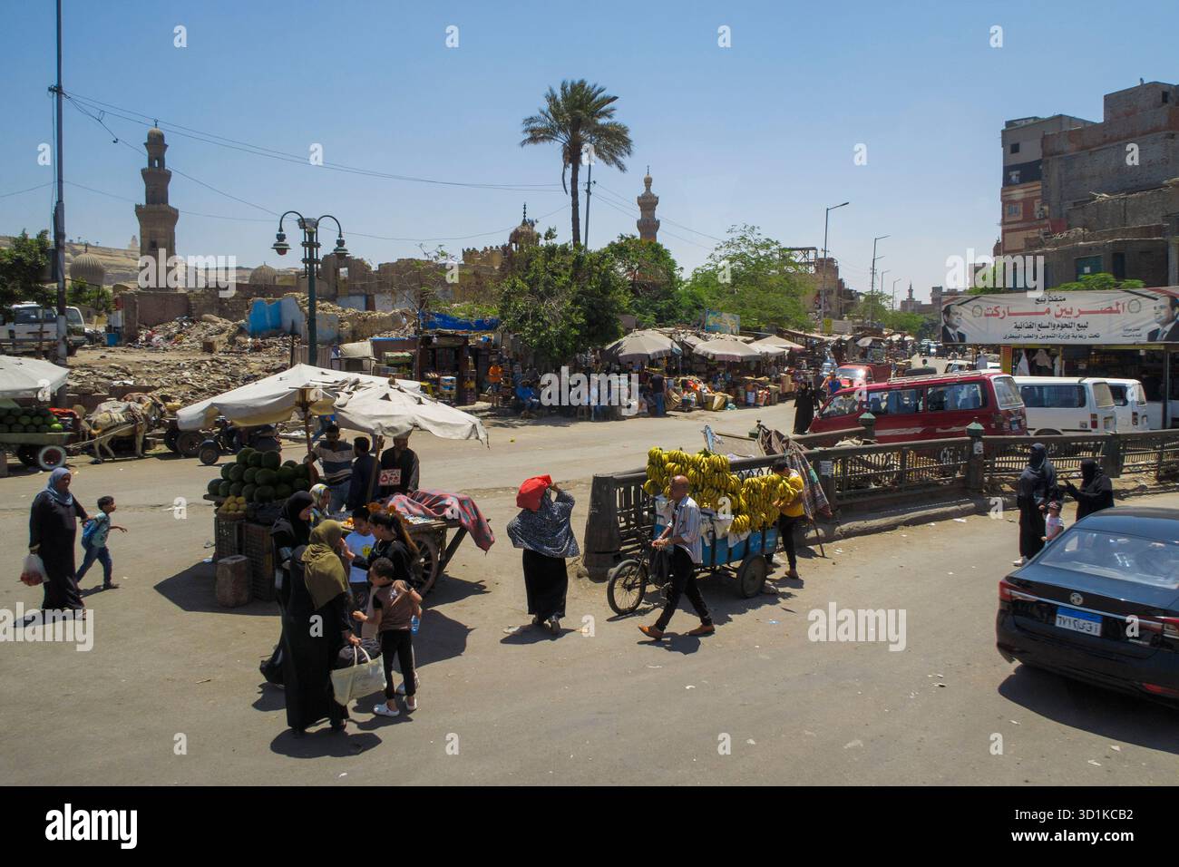 Vivace mercato di strada al Cairo, in Egitto, con gente che fa shopping, venditori di frutta e minareti sullo sfondo sotto un cielo soleggiato Foto Stock