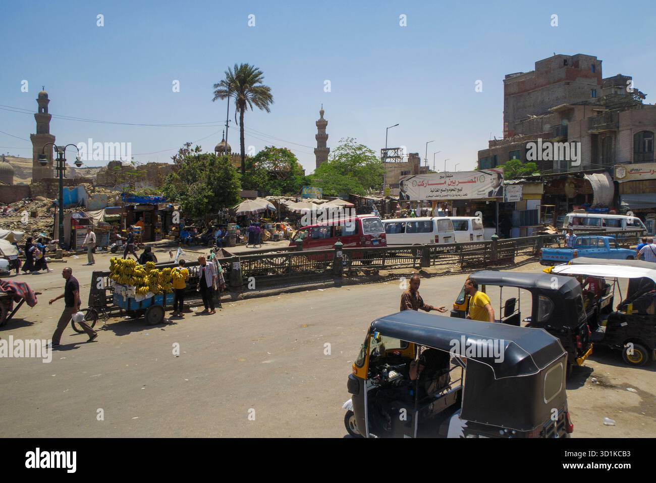 Vivace mercato di strada al Cairo, in Egitto, con gente che fa shopping, venditori di frutta e minareti sullo sfondo sotto un cielo soleggiato Foto Stock