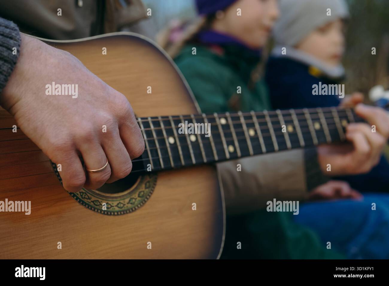 vista ravvicinata delle mani dell'uomo che suona una chitarra acustica. due bambini sullo sfondo. Picnic in famiglia in autunno. Foto di alta qualità Foto Stock