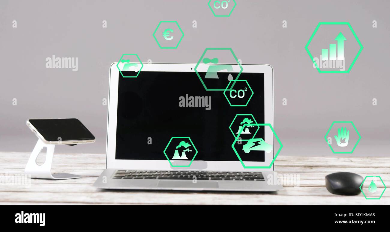 Computer portatile argento seduto su una scrivania in legno in ufficio, con supporto per smartphone, mouse e icone verdi Foto Stock