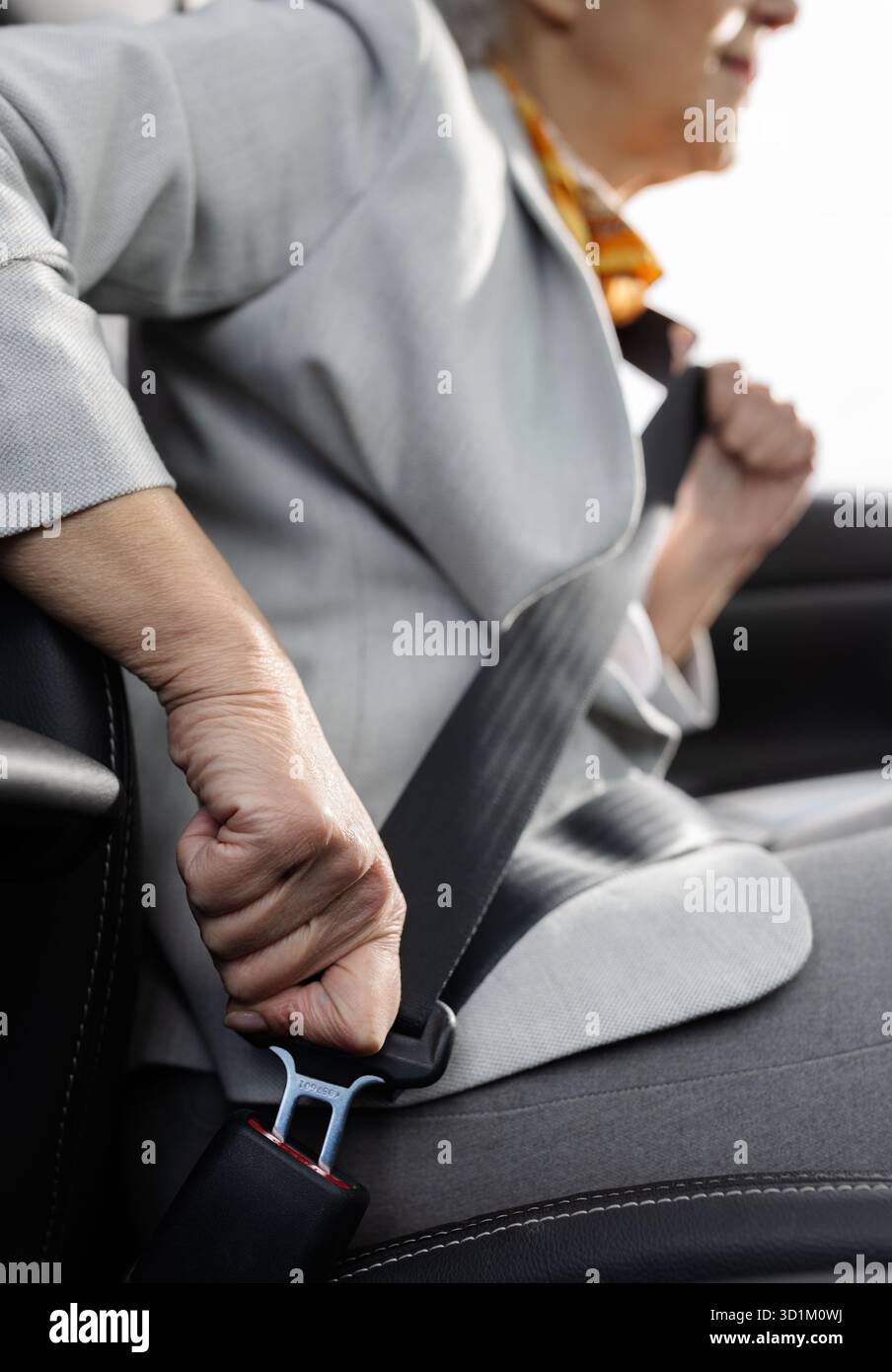 Una donna anziana siede in auto e fissa la cintura di sicurezza mentre si prepara a guidare, dimostrando consapevolezza della sicurezza e disponibilità per il viaggio che ci attende. Foto Stock