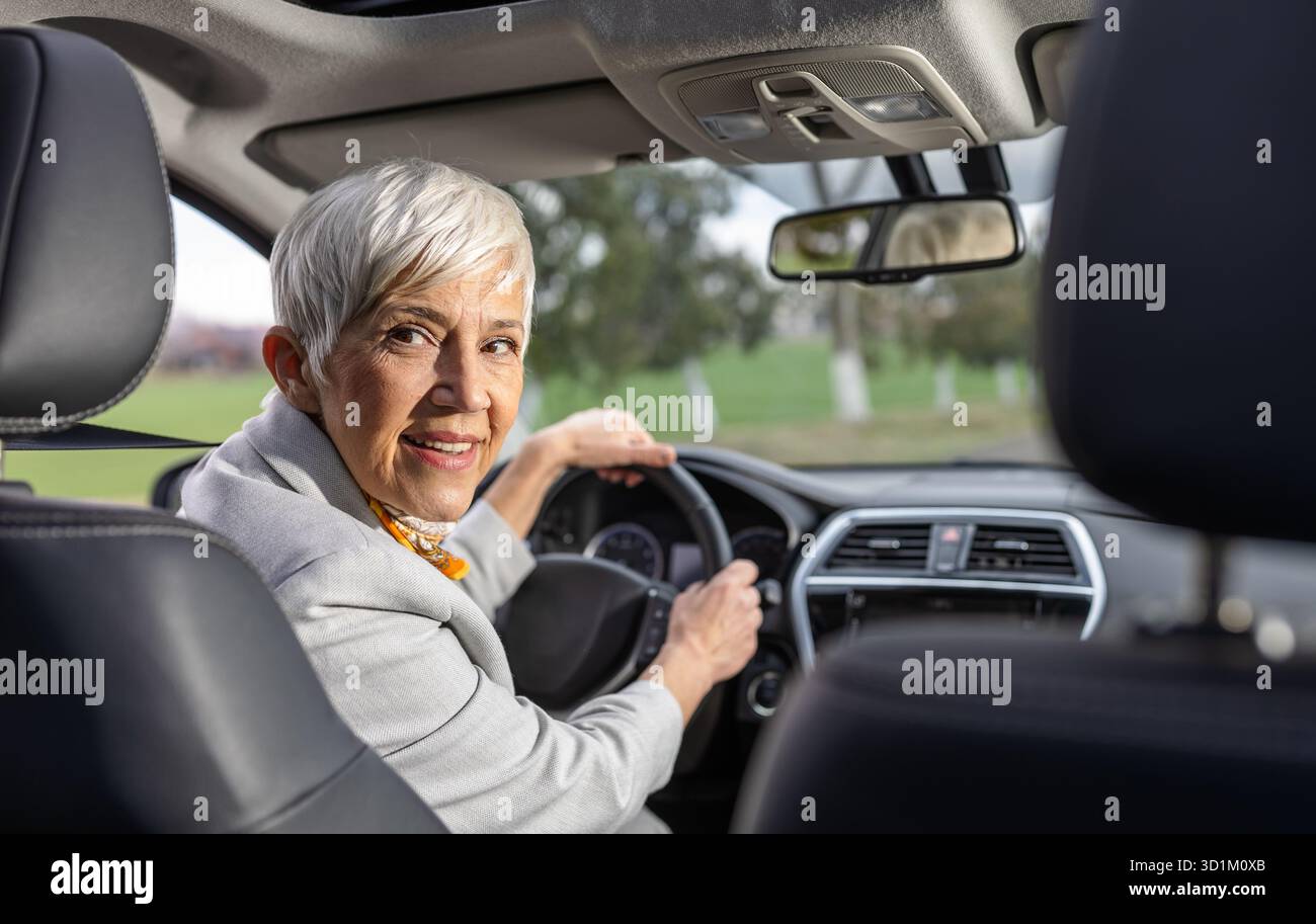 Donna anziana sorridente seduta in macchina e che guarda indietro sul sedile Foto Stock