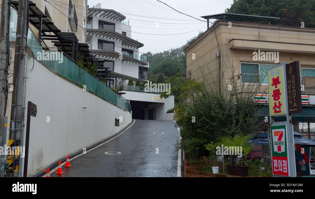 SEOUL, COREA DEL SUD - 11 OTTOBRE 2025 - Una strada nel villaggio di Achiul, Seoul, che mostra edifici moderni e un 7 undici in un giorno di pioggia Foto Stock