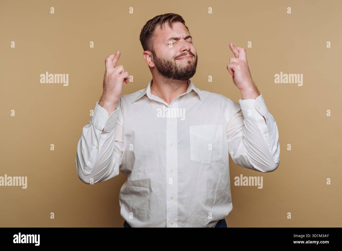 Uomo con barba che incrocia le dita e gli occhi di chiusura, sperando in fortuna. Foto Stock