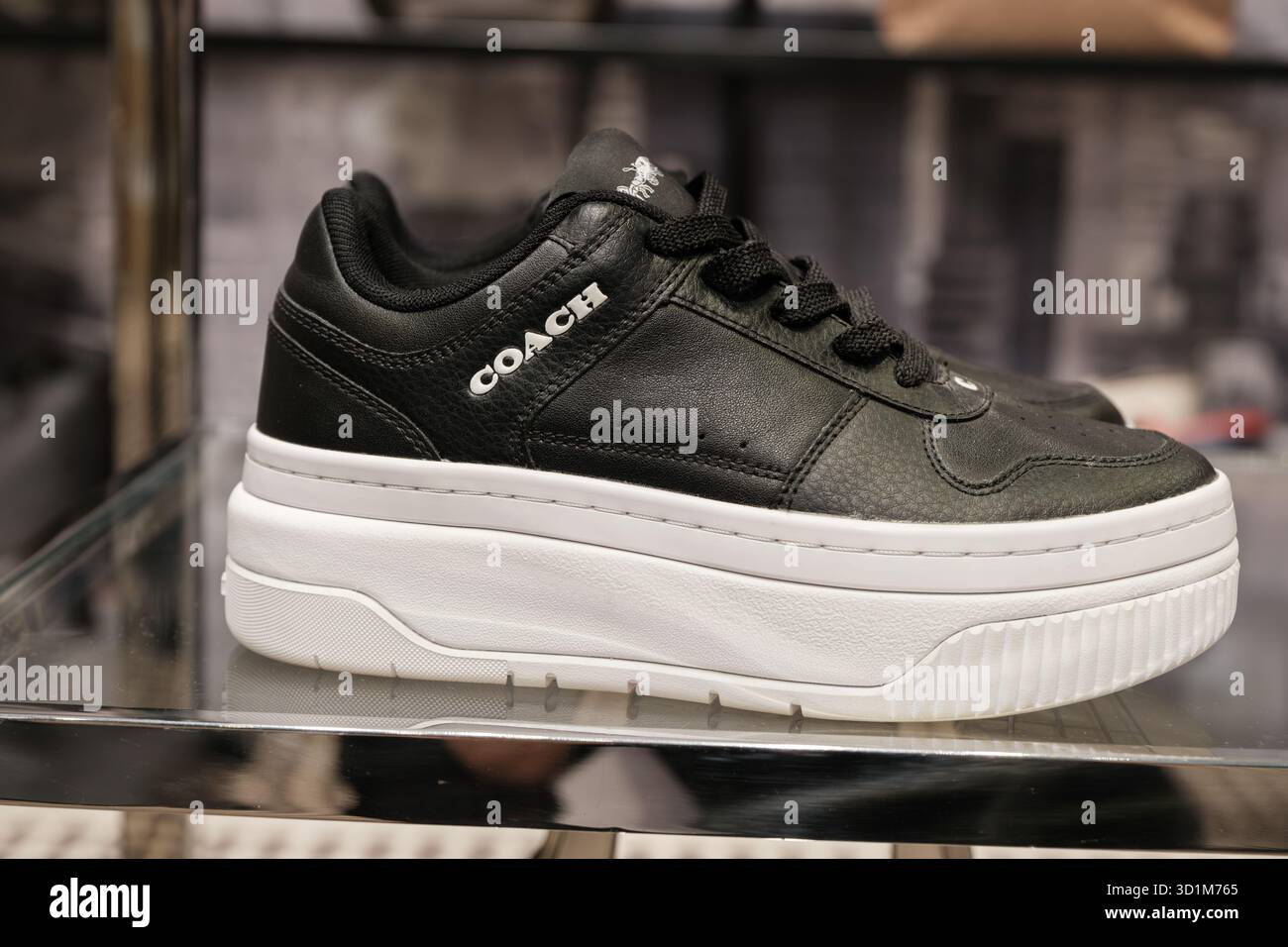 Le sneaker Coach con plateau in pelle nera sono caratterizzate da una suola bianca e sono esposte su uno scaffale in vetro in un ambiente di vendita al dettaglio con soffusa illuminazione superiore. Foto Stock