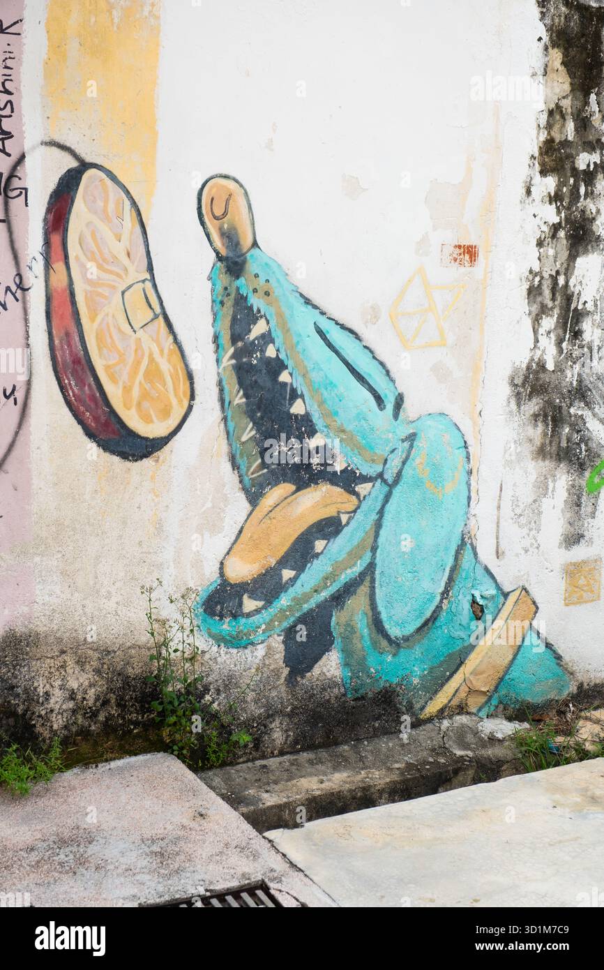 Un vivace murale di coccodrillo con un'espressione giocosa, che raggiunge una grande fetta di frutta, esalta il paesaggio urbano con un tocco artistico. Foto Stock