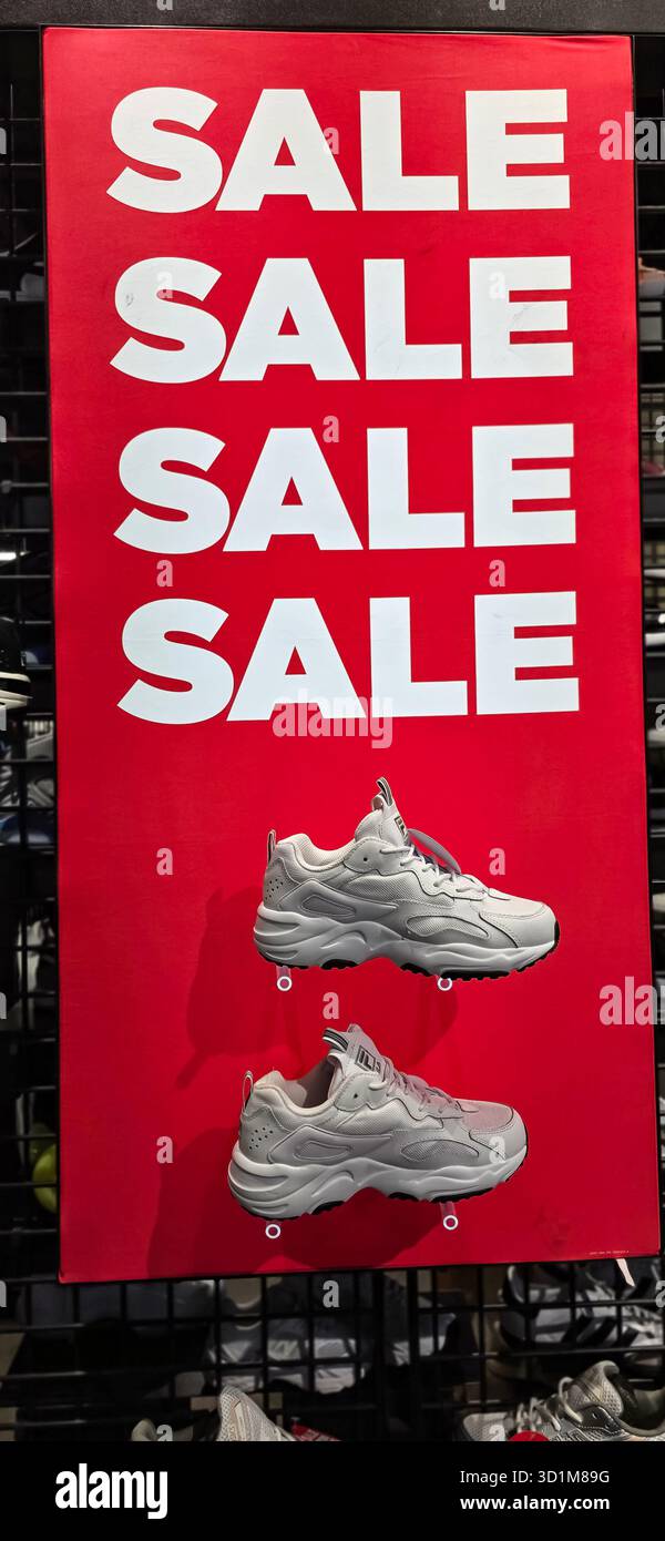 Berlino, Germania - 13 giugno 2025: Scarpe da atletica bianche in mostra sul manifesto rosso vivace dei saldi in negozio. Foto Stock