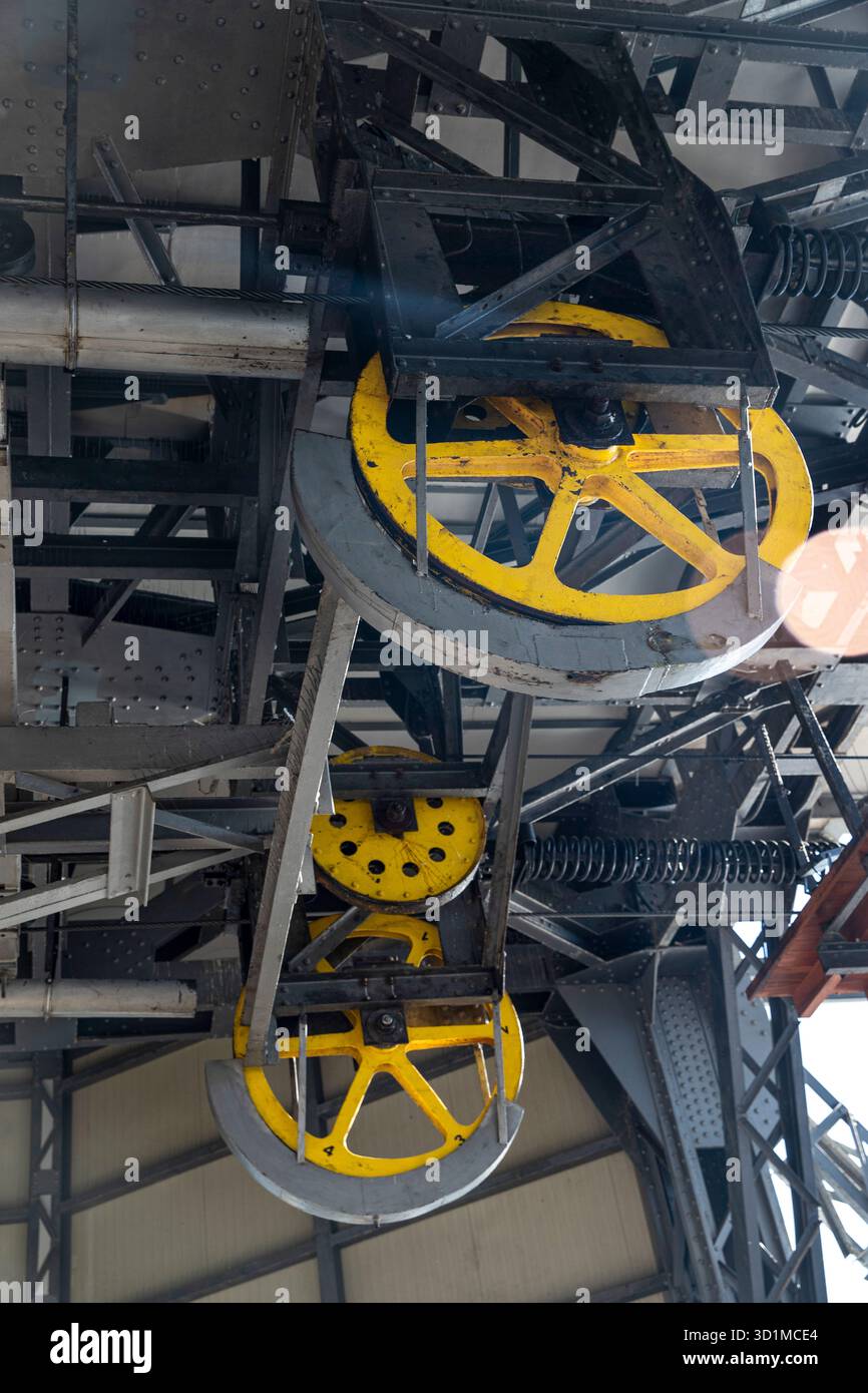 Struttura ingegneristica: Un sistema di pulegge e cavi per lo spostamento di una cabina di sollevamento. Vecchio meccanismo industriale, primo piano di una ruota gialla da più tonnellate Foto Stock