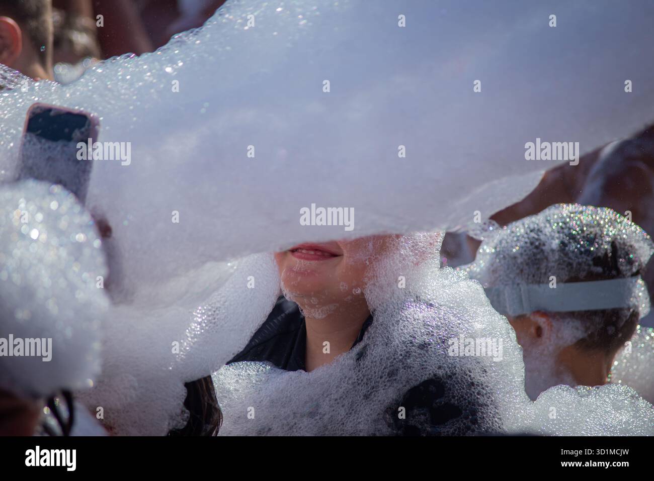 Le bolle di schiuma coprono i volti sorridenti in una vivace festa di schiuma a Hurghada, in Egitto. Le persone apprezzano l'atmosfera giocosa, circondata da strati spessi di schiuma Foto Stock