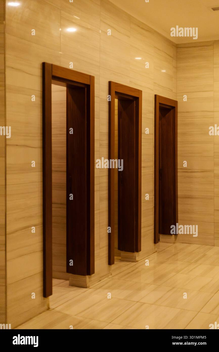 Un tranquillo corridoio presenta tre telai delle porte in legno sullo sfondo di marmo liscio e di colore chiaro. L'illuminazione calda crea un'atmosfera tranquilla. Foto Stock
