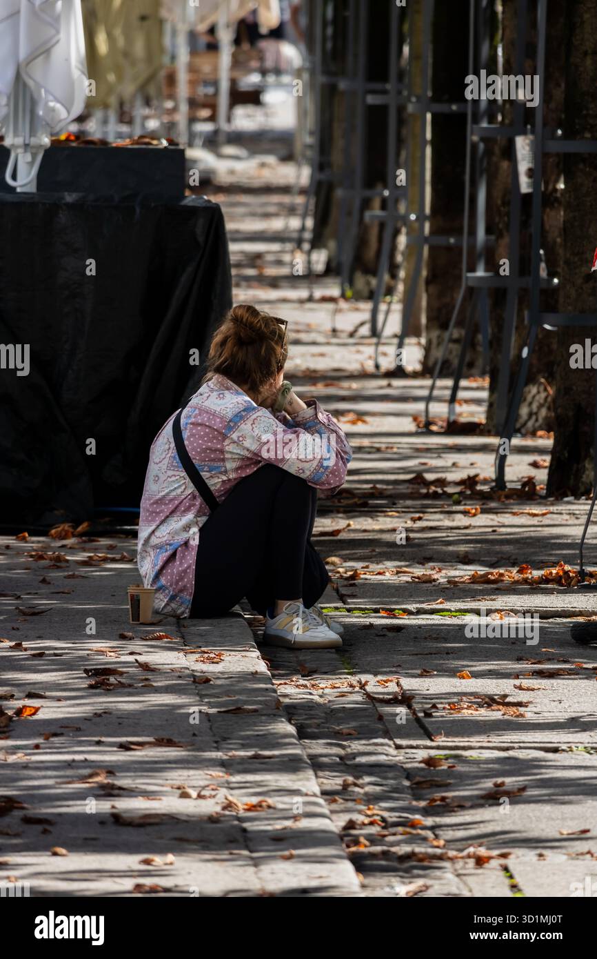 Lubiana, Slovenia 30 agosto 2025 persona seduta all'aperto tra foglie cadute, sfondo urbano autunnale Foto Stock