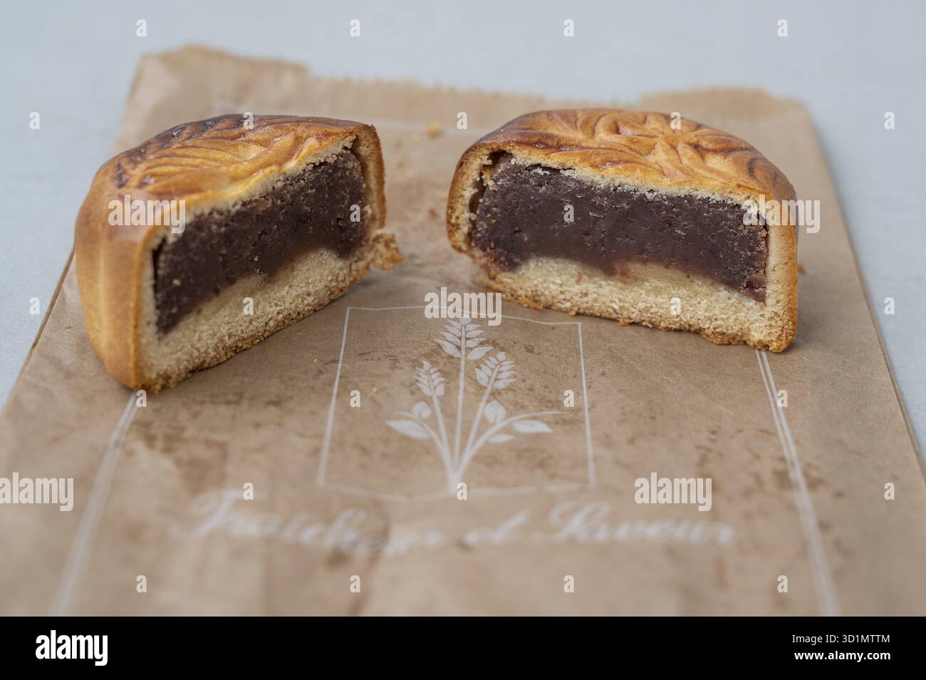 Primo piano di una Mooncake (Mooncake) tagliata al centro con uno strato spesso di pasta di fagioli rossi scuri e una base di pasta frolla leggera, presentata su una crosta marrone Foto Stock