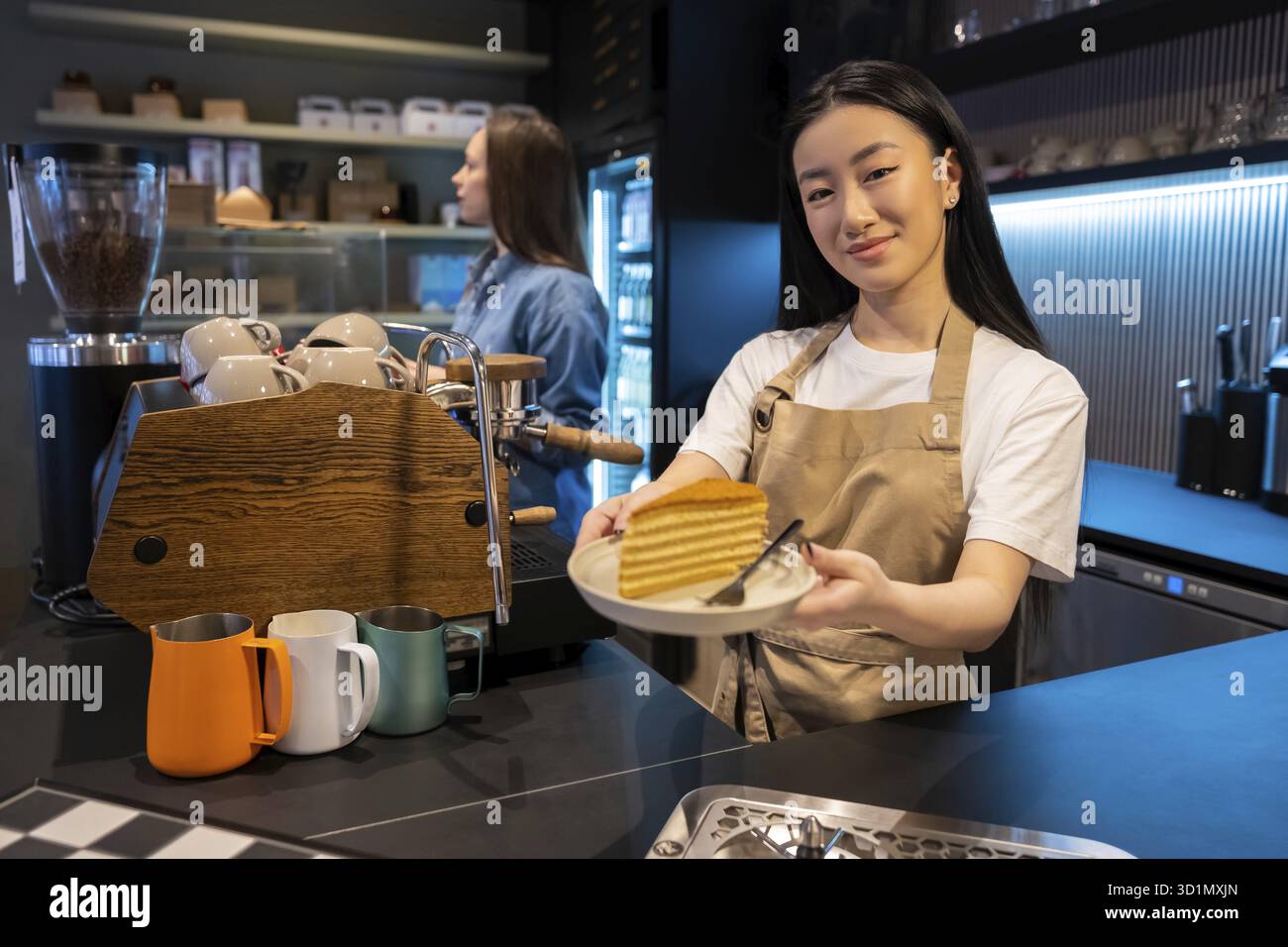 Un'amichevole dipendente del bar che consegna una fetta di torta a un cliente in presenza della sua collega Foto Stock