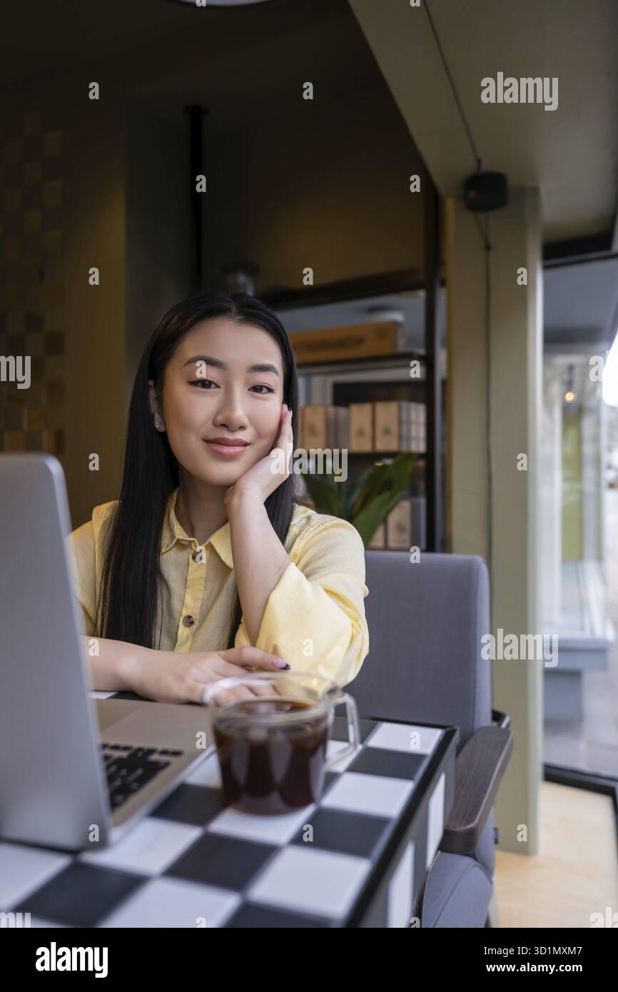 Calma giovane donna asiatica seduta di fronte al computer portatile in una caffetteria Foto Stock