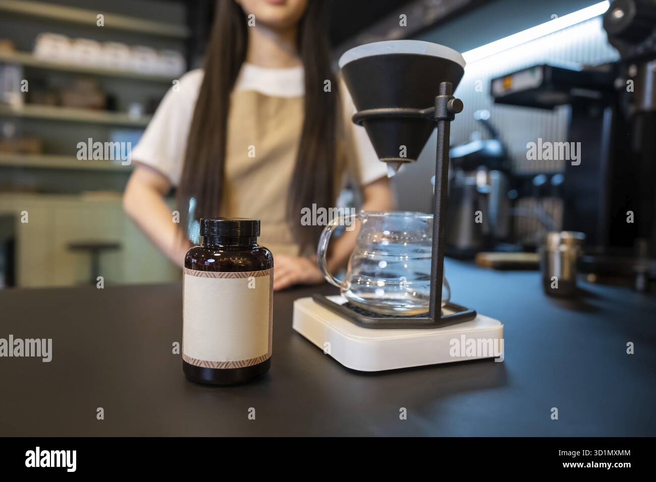 Primo piano di una bottiglia di plastica e di una macchina per il caffè con funzione "pour-over", messi sul bancone e un addetto al bar Foto Stock