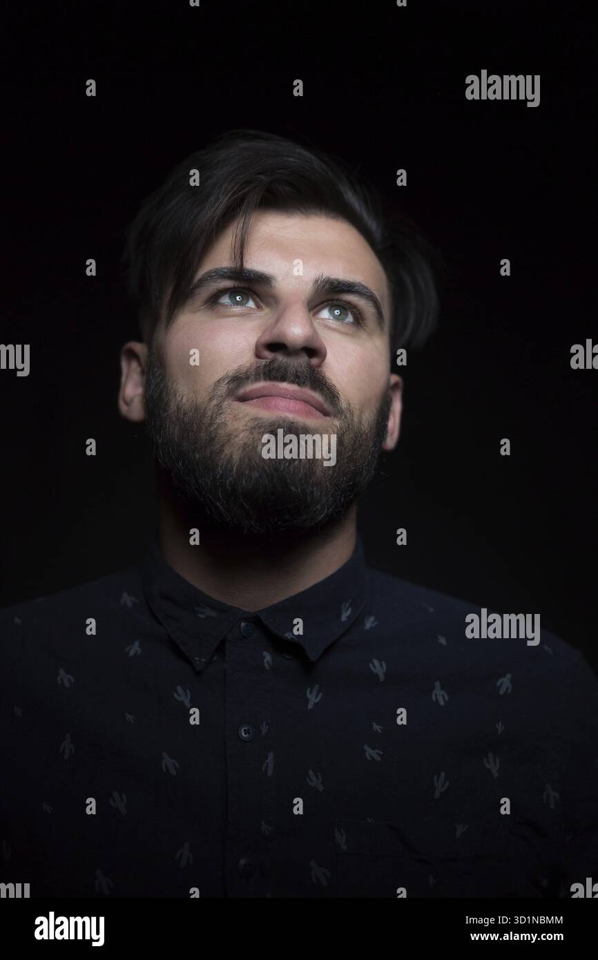Ritratto chiave bassa di un giovane uomo bello in camicia scura isolata su sfondo nero Foto Stock