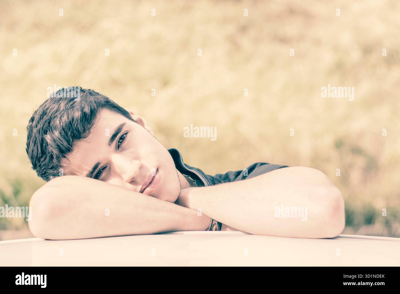 Giovane che guarda la macchina fotografica all'aperto, appoggiato con la testa appoggiata sulle mani Foto Stock