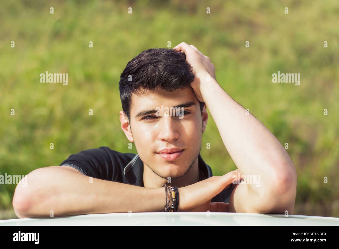 Giovane che guarda la macchina fotografica all'aperto, appoggiato con la testa appoggiata sulle mani Foto Stock