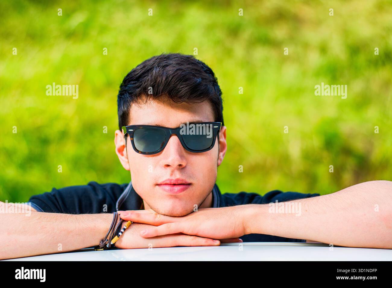 Giovane che guarda la macchina fotografica all'aperto, appoggiato con la testa appoggiata sulle mani Foto Stock