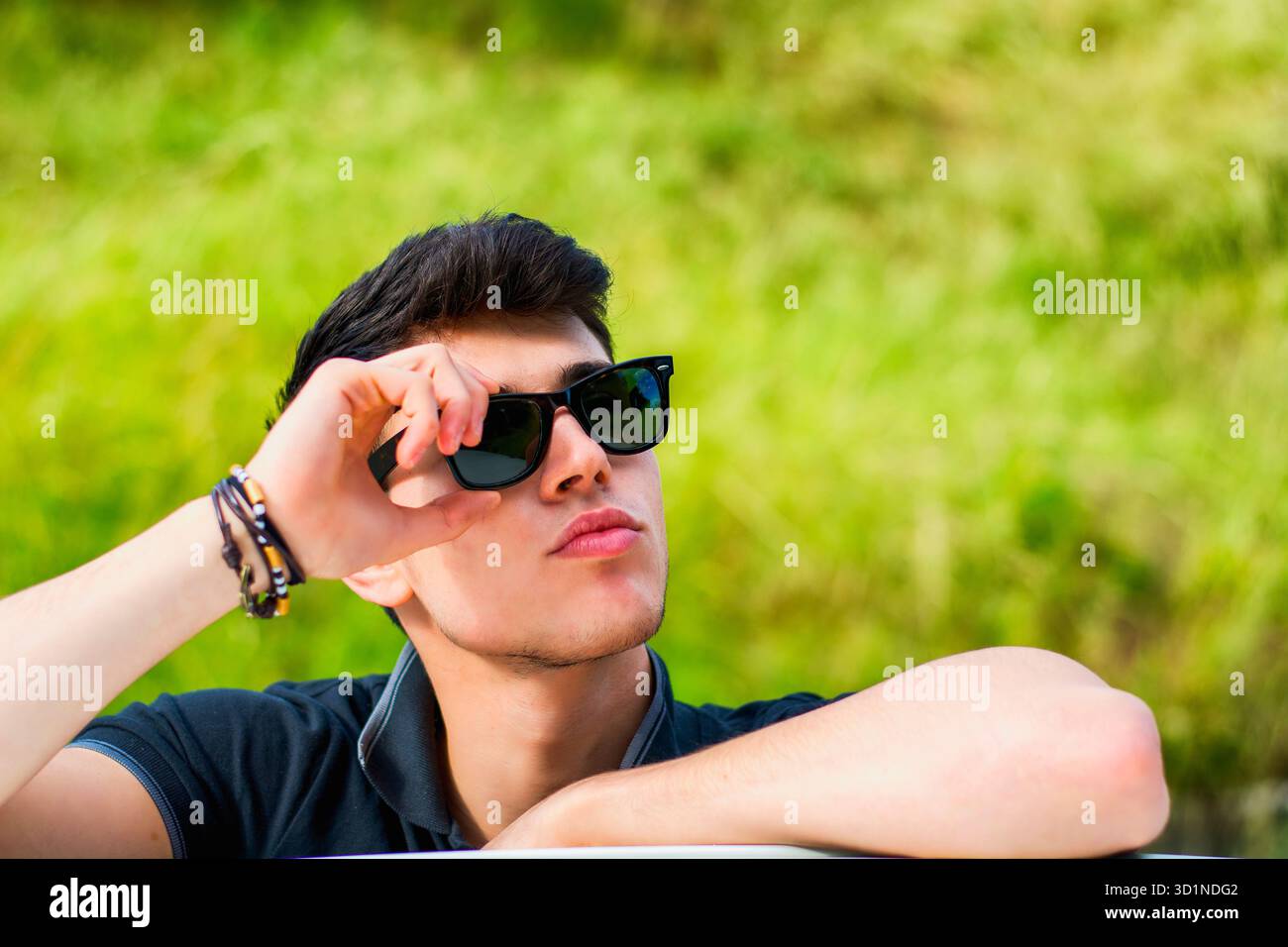 Giovane che guarda la macchina fotografica all'aperto, appoggiato con la testa appoggiata sulle mani Foto Stock