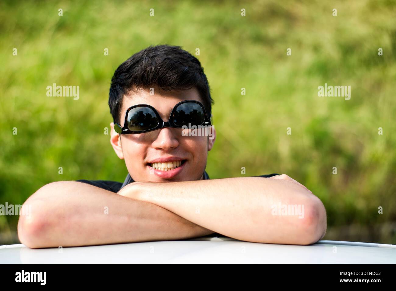 Giovane che guarda la macchina fotografica all'aperto, appoggiato con la testa appoggiata sulle mani Foto Stock