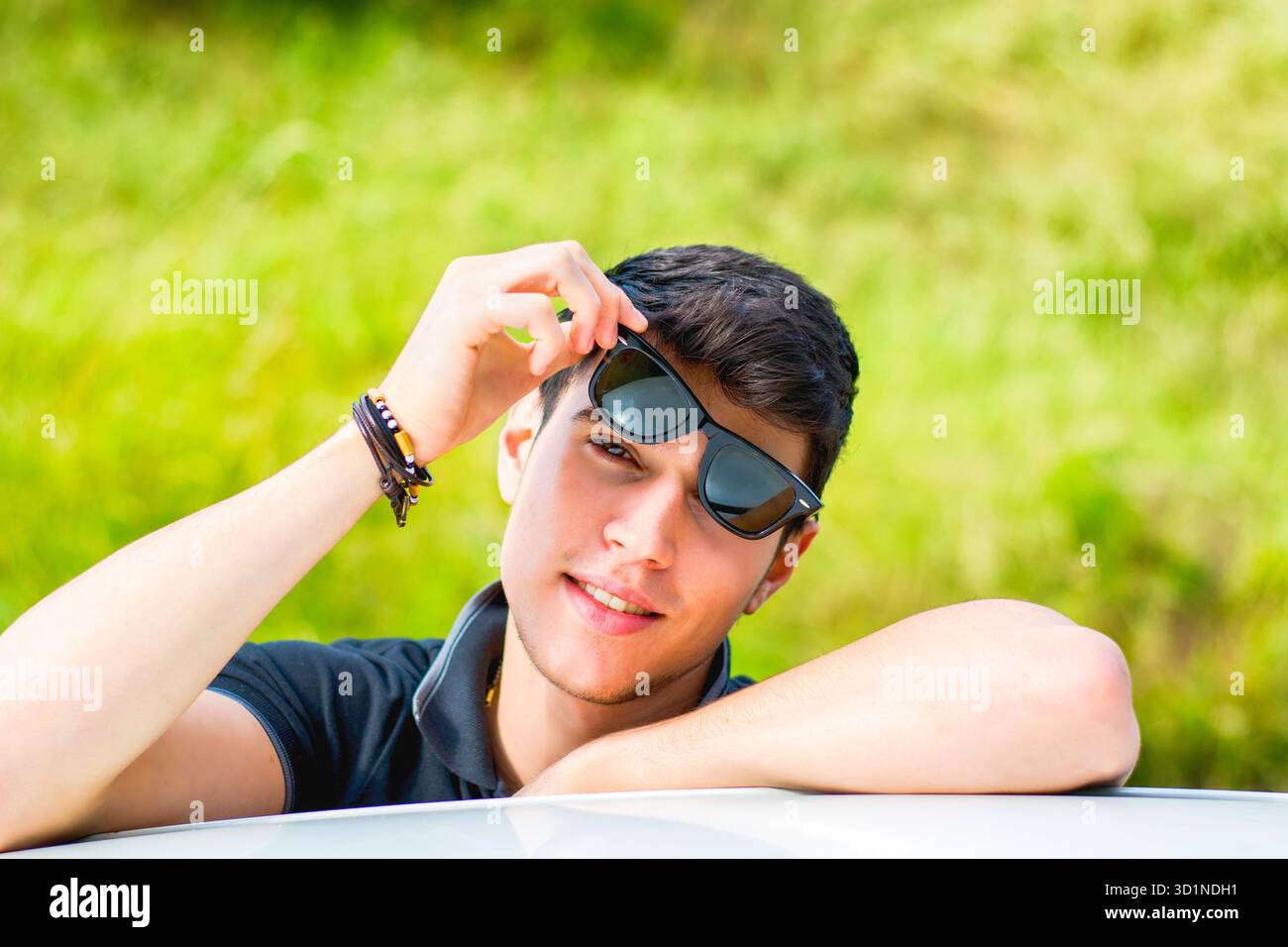 Giovane che guarda la macchina fotografica all'aperto, appoggiato con la testa appoggiata sulle mani Foto Stock