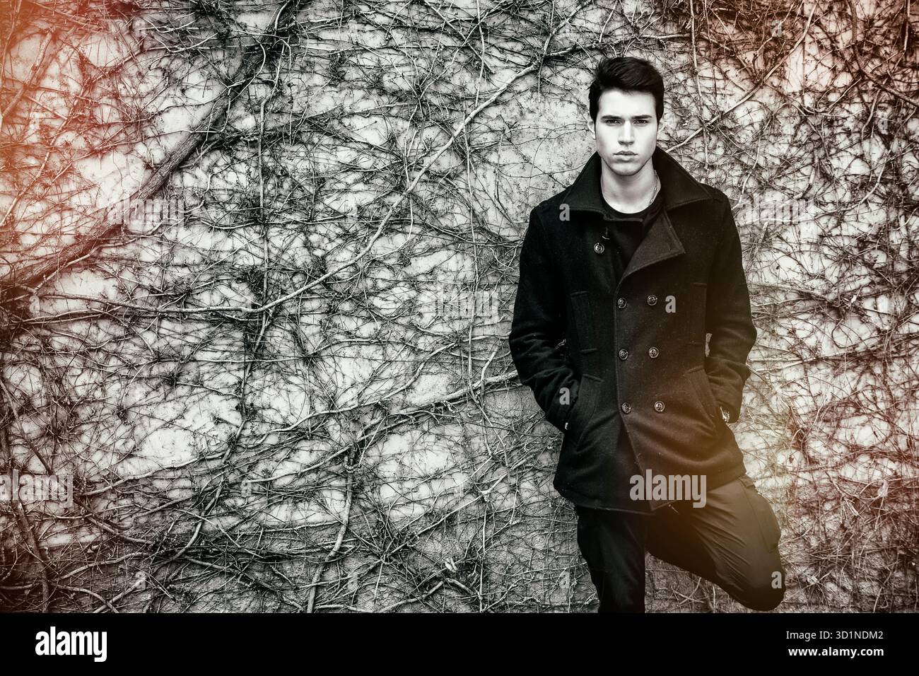 Bel giovane uomo in piedi contro un muro coperto di piante Foto Stock