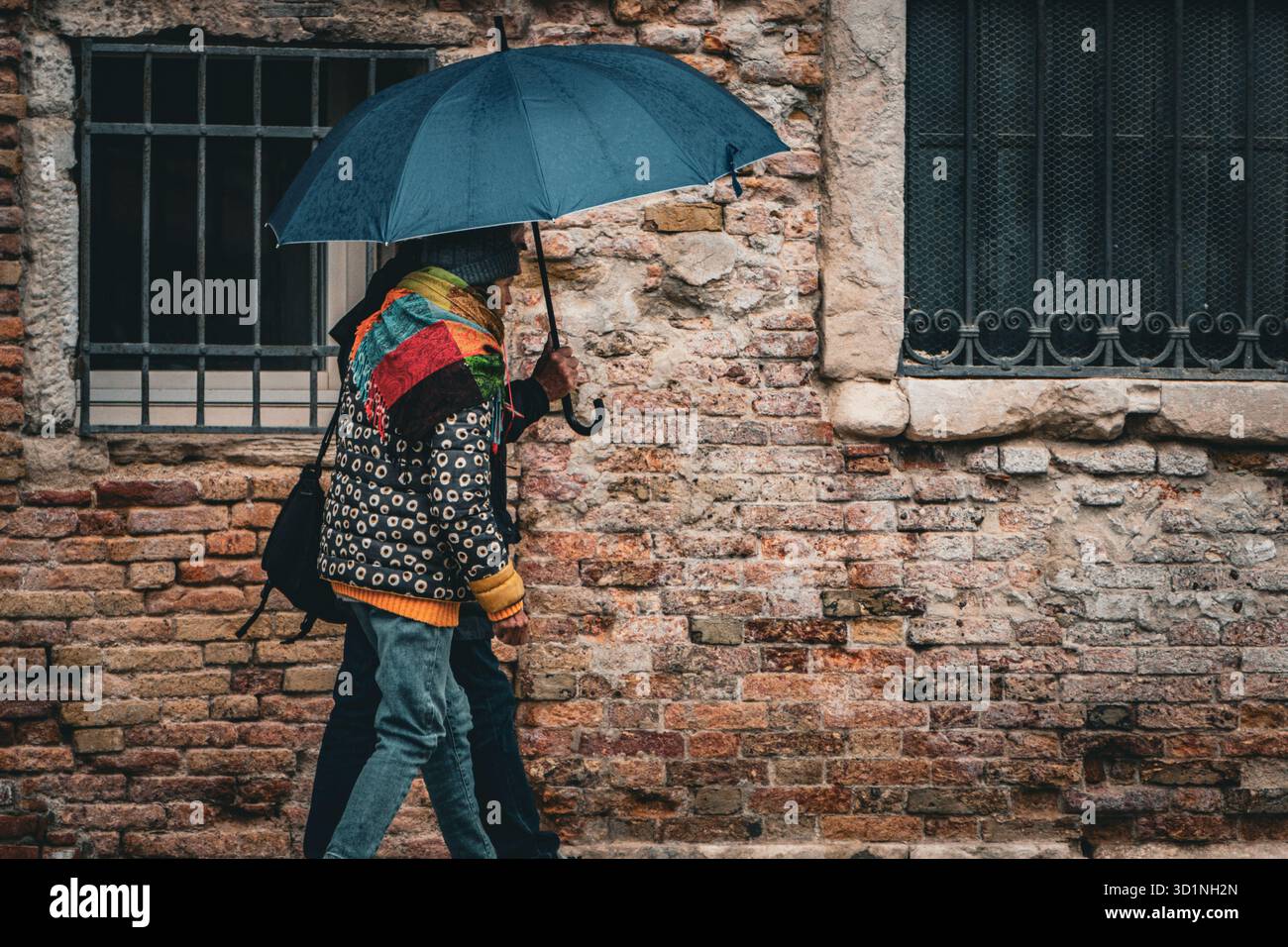 Una coppia che cammina con un ombrello blu accanto a un vecchio muro di mattoni a Venezia, Italia Foto Stock