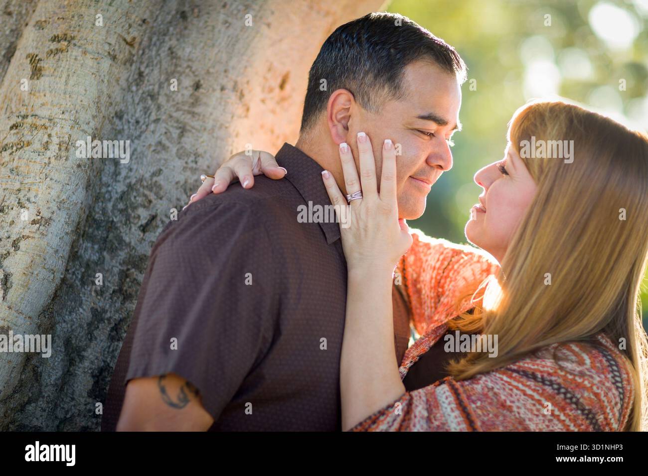 Coppia di corsa mista appoggiata contro l'albero in un momento romantico Foto Stock