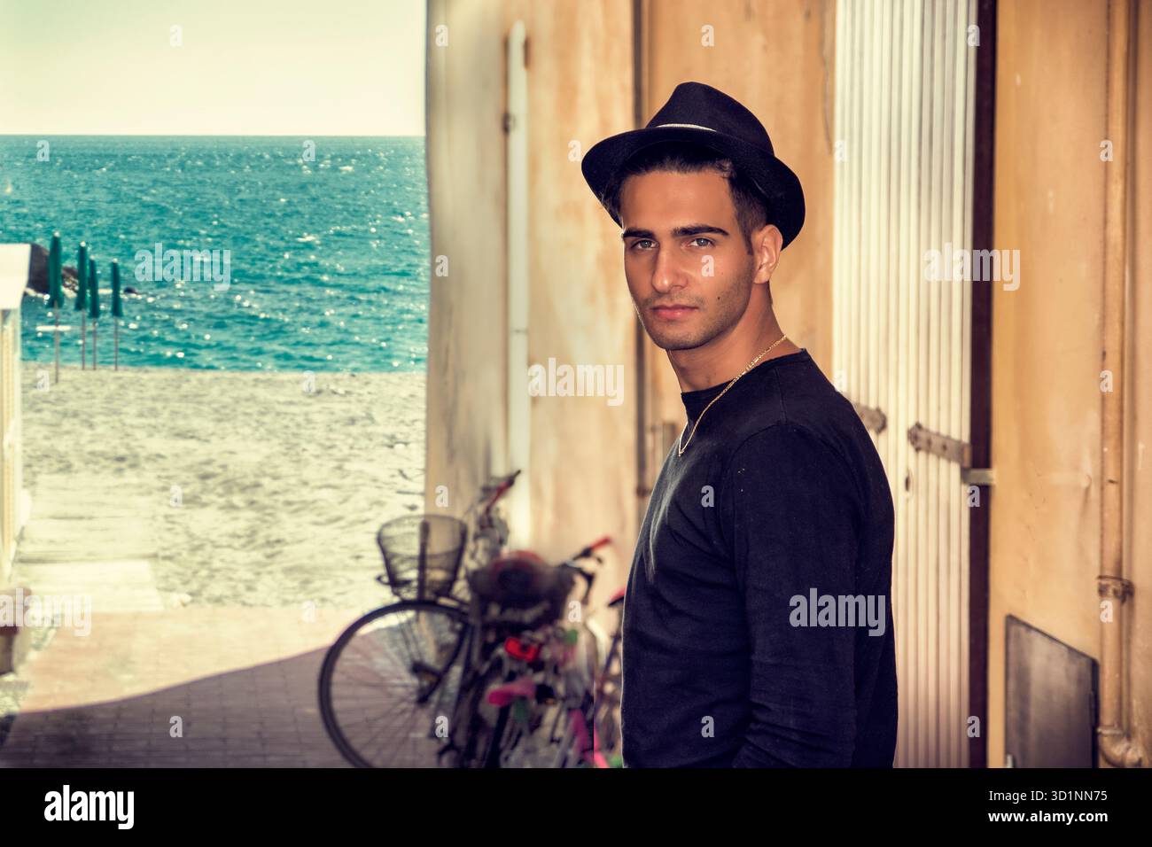Uomo con cappello nero in piedi vicino al muro mentre guarda la fotocamera Foto Stock
