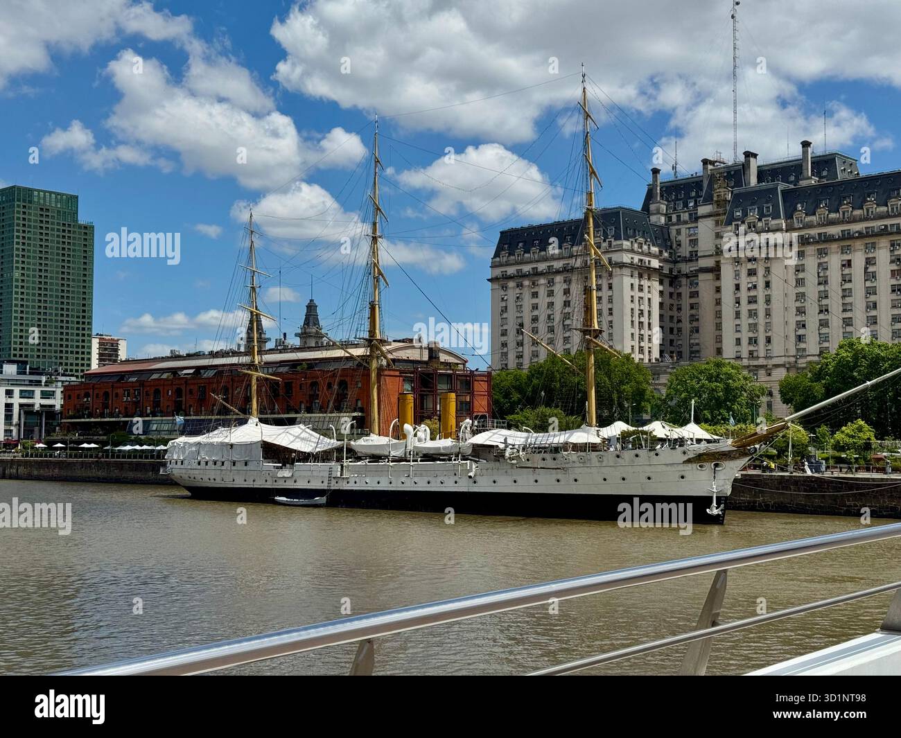Storico veliero bianco ormeggiato sulle acque marroni del molo di Puerto Madero con un grande edificio storico e moderni grattacieli sullo sfondo - Immagine stock catturata con smartphone