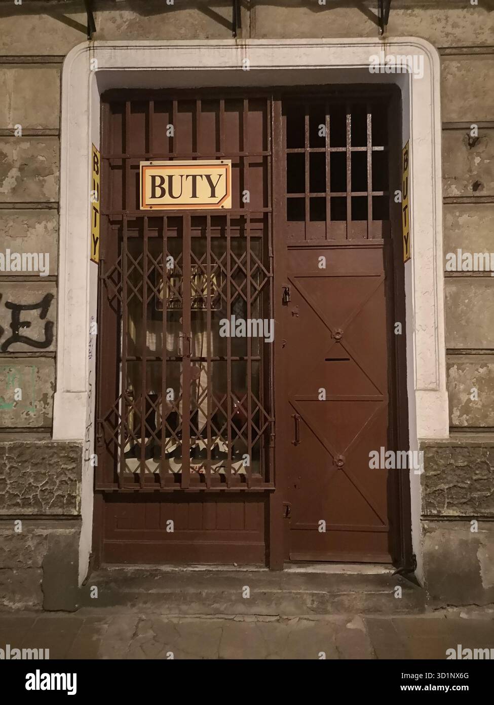 Il tradizionale negozio di scarpe vecchio stile con cancelli in ferro si aggrava di notte: Il fascino tranquillo di Kazimierz persiste ancora nello storico quartiere ebraico di Kraków. - Immagine stock catturata con smartphone