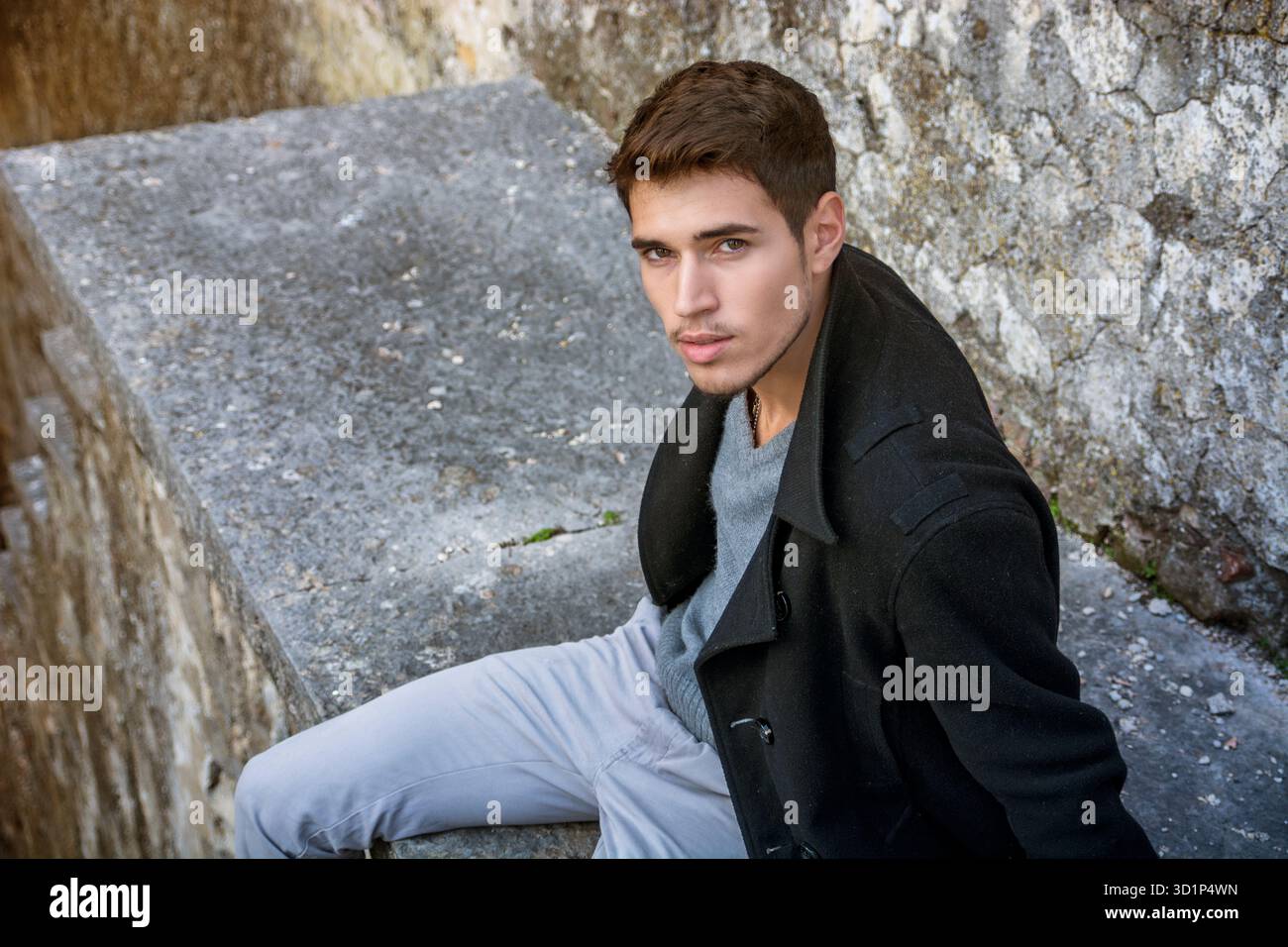 Ritratto di un uomo dai capelli neri seduto sul bordo di pietra e che guarda lontano Foto Stock