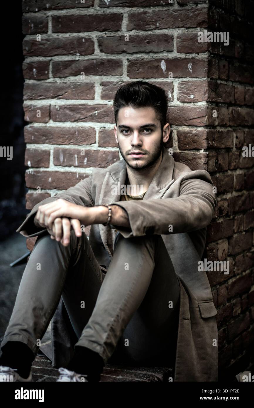 Un giovane attraente seduto contro un muro di mattoni Foto Stock