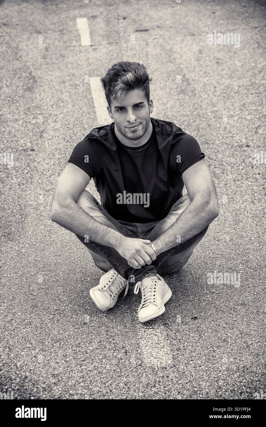 Un uomo sorridente seduto in mezzo alla strada della città Foto Stock
