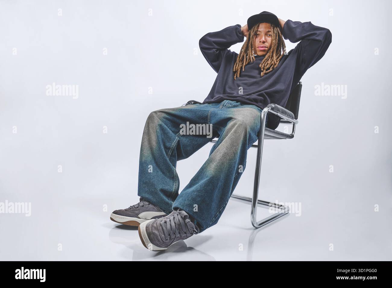 Giovane uomo con dreadlock seduti su una sedia, che mette in mostra lo streetwear urbano e la moda casual Foto Stock