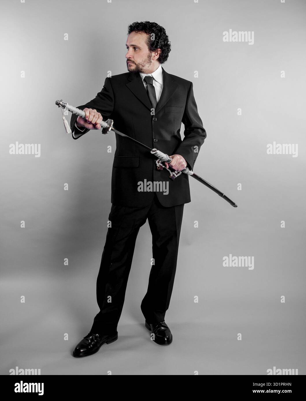 Imprenditore di difesa in abito nero e armati di spada giapponese su sfondo grigio Foto Stock