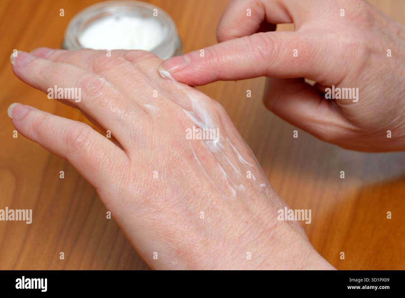 Mani che applicano un ricco idratante sulla pelle per idratazione e morbidezza. Foto Stock
